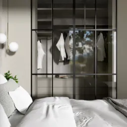 Sypialnia z łóżkiem z szarą tapicerką i pościelą w odcieniach bieli i szarości, na ścianie lampa z dwoma białymi kulami, w tle przeszklona szafa z ubraniami.