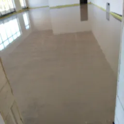 Świeżo wylana, jasna wylewka anhydrytowa w przestronnym pomieszczeniu z widocznymi oknami i żółtą taśmą zabezpieczającą przy ścianach.