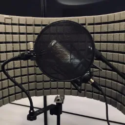 Mikrofon studyjny z filtrem pop i ekranem akustycznym z pianki, ustawiony w zacisznym kącie studia nagrań.