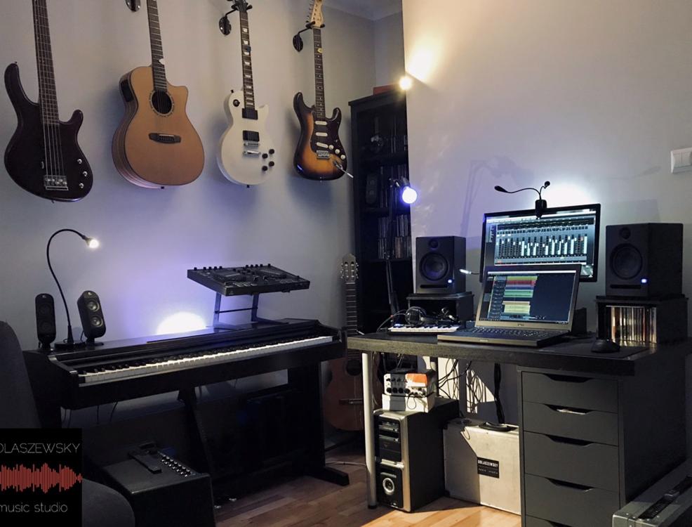 Domowe studio nagrań z cyfrowym pianinem, komputerem z oprogramowaniem DAW, monitorami studyjnymi i kolekcją gitar wiszących na ścianie.