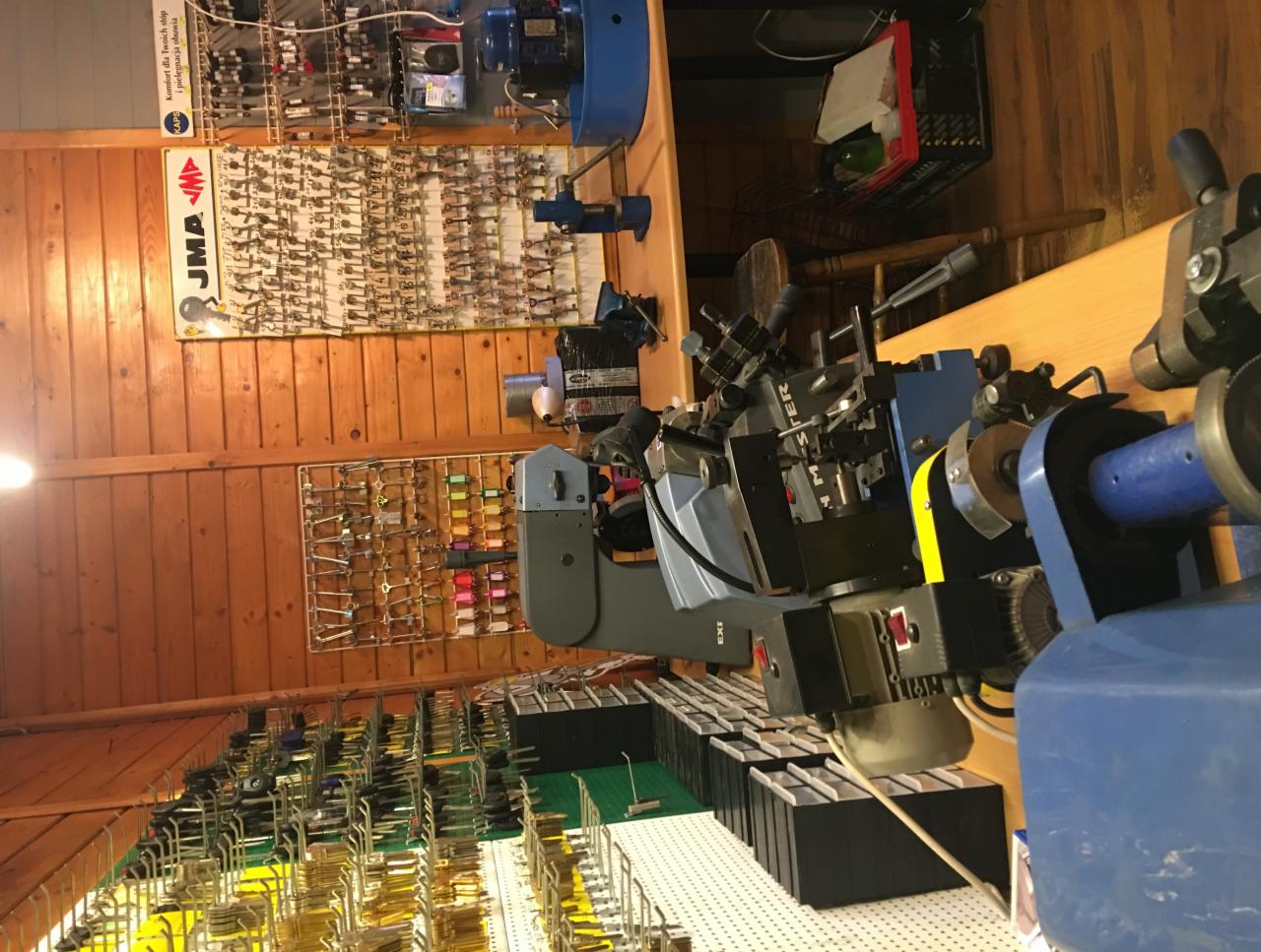 Warsztat ślusarski: maszyna do kopiowania kluczy, ściana z ekspozycją różnorodnych kluczy, drewniane panele ścienne.