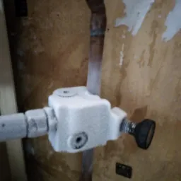 Zamarznięty zawór i rura miedziana wewnątrz budynku, z widocznymi śladami wilgoci na ścianie.