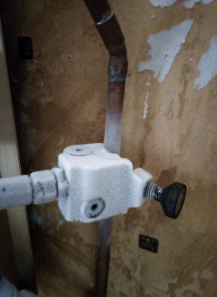 Zamarznięty zawór i rura miedziana wewnątrz budynku, z widocznymi śladami wilgoci na ścianie.
