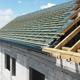 Budowa dachu domu jednorodzinnego w trakcie realizacji: widoczne krokwie, łaty, membrana dachowa i orynnowanie na surowej konstrukcji budynku.