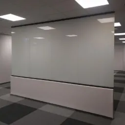 Szklana ścianka działowa w biurze, z białym cokołem i czarną ramą, widoczne odbicia lamp sufitowych.