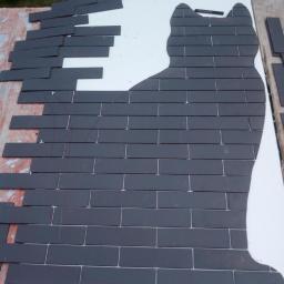 Damian Tychulski - Układanie ciemnoszarych płytek w kształcie kota na białej płycie, widoczne linie cięcia i luźne płytki po lewej stronie.