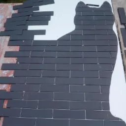 Układanie ciemnoszarych płytek w kształcie kota na białej płycie, widoczne linie cięcia i luźne płytki po lewej stronie.