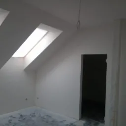 Poddasze po remoncie: gładkie, białe ściany z dwoma oknami dachowymi i przygotowanym otworem na drzwi. Folia ochronna na podłodze.