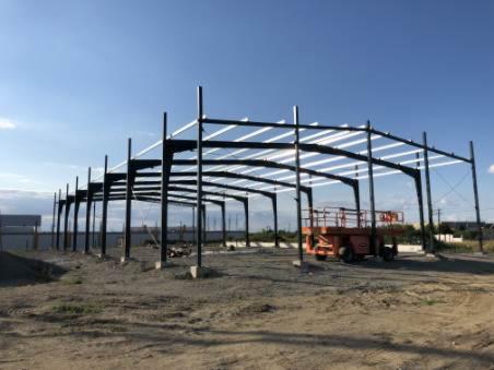 Konstrukcja stalowa hali w trakcie budowy, widoczny podnośnik koszowy na placu budowy, słoneczny dzień.