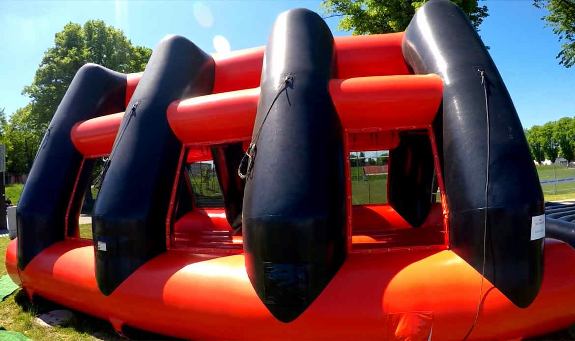 Pompowany tor przeszkód w kolorach czarnym i czerwonym, z widocznymi elementami mocującymi i otoczeniem zieleni.