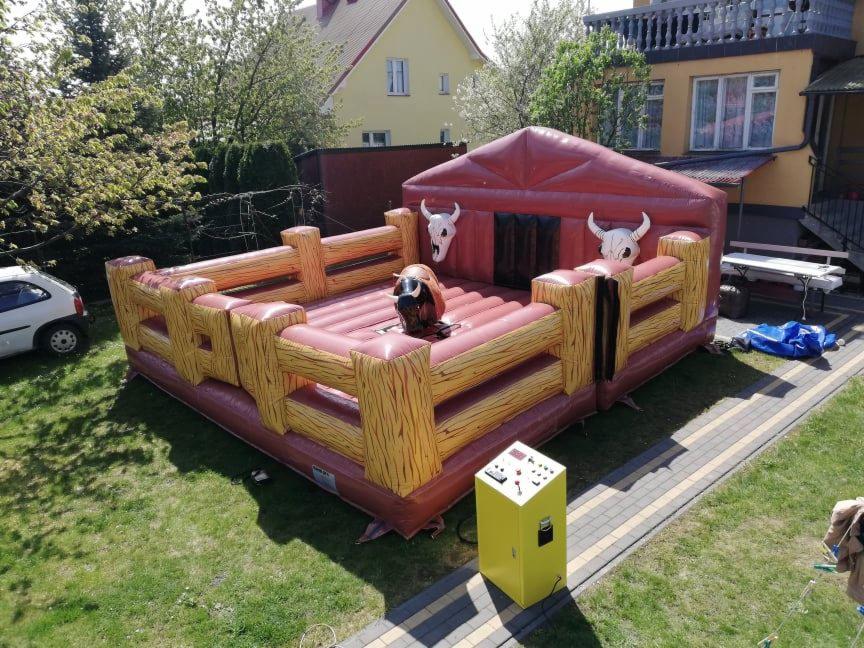 Nadmuchiwania atrakcja rodeo z elektrycznym panelem sterowania na trawie przed domem z żółtą elewacją.