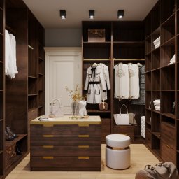 Dekorroom - Przestronna garderoba z ciemnego drewna, z wysuwana komodą z jasnym blatem, białym pufem i dekoracjami, oświetlona punktowymi lampami sufitowymi.