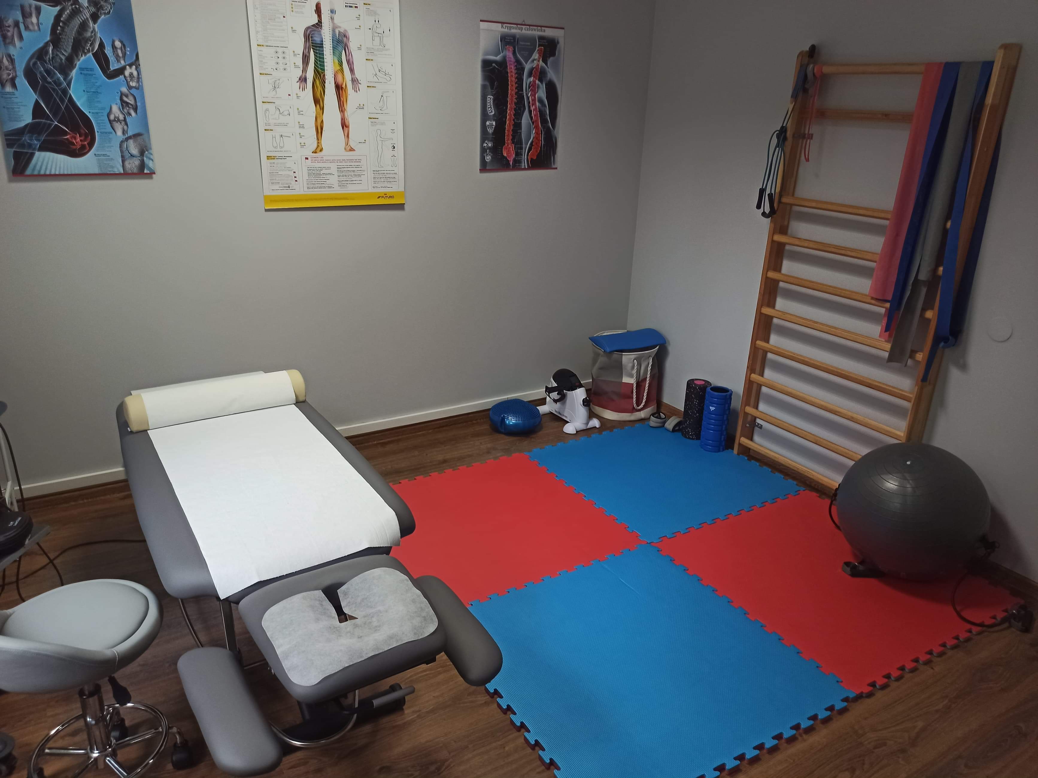 Gabinet z kozetką, drabinką gimnastyczną i plakatami anatomicznymi na ścianach, przygotowany do zabiegów.