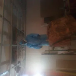 Pracownik w kombinezonie ochronnym montuje izolację z wełny mineralnej w metalowym stelażu ściany działowej, widoczne elementy rusztowania.