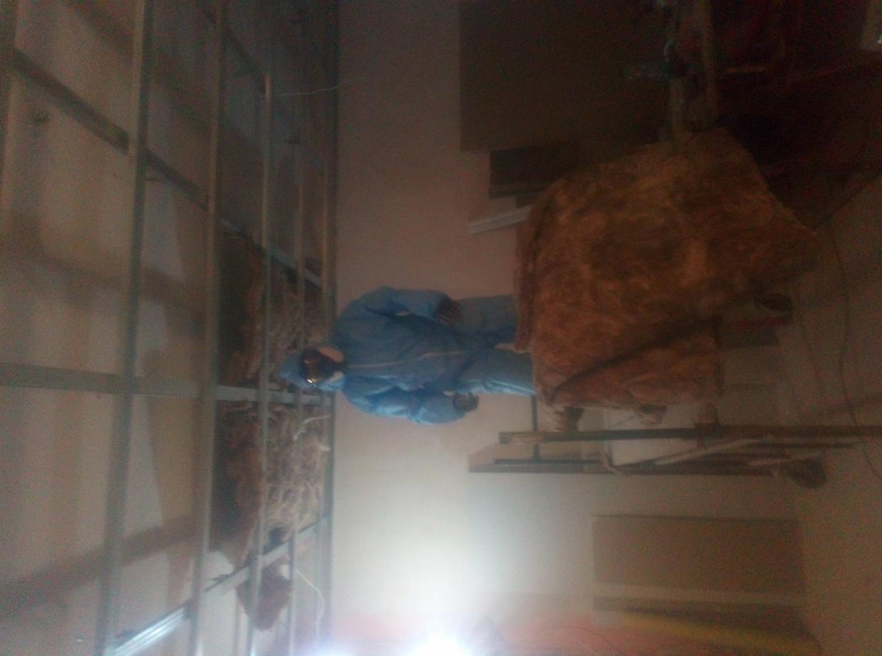 Pracownik w kombinezonie ochronnym montuje izolację z wełny mineralnej w metalowym stelażu ściany działowej, widoczne elementy rusztowania.