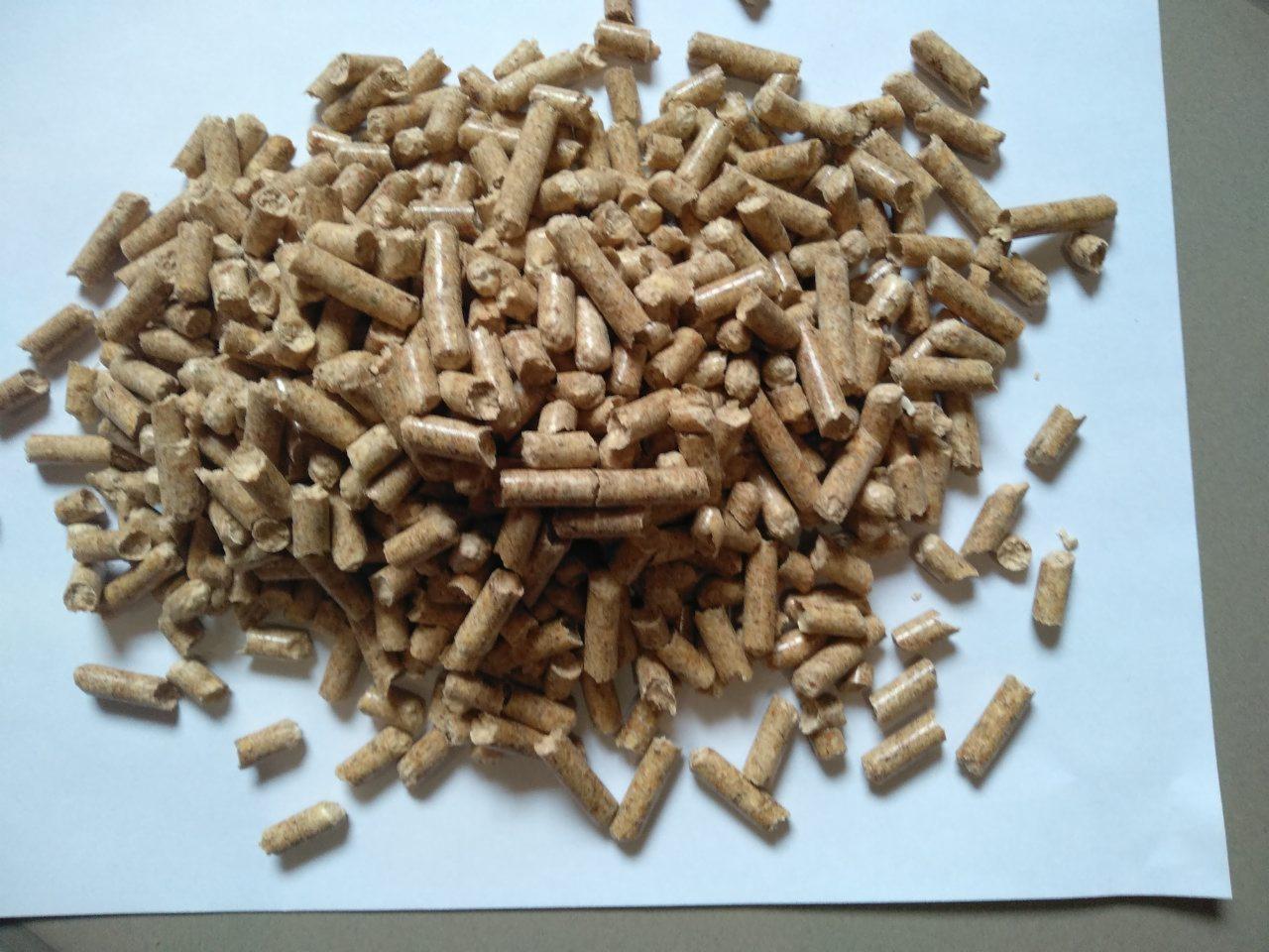 Stos brązowych pelletów drzewnych na białym tle, widoczne struktury drewna i drobne wióry.