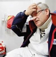 Zamyślony mężczyzna w okularach, ubrany w strój roboczy, dotyka czoła dłonią. Widoczne elementy stroju roboczego i wyposażenia w tle sugerują pracę związaną z instalacjami.