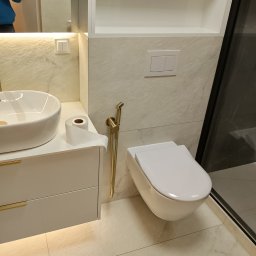 BART-HAUS - Nowoczesna łazienka z umywalką nablatową, toaletą podwieszaną i złotą armaturą. Białe meble z podświetleniem LED i marmurowe płytki tworzą elegancki wystrój.