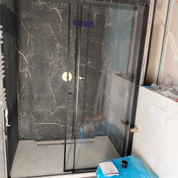 BART-HAUS - Nowoczesna kabina prysznicowa z czarnymi profilami i marmurowymi płytkami. Widoczny odpływ liniowy i częściowo zakryta toaleta.