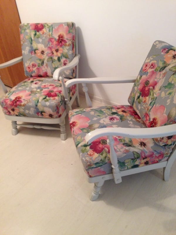 Dwa odnowione fotele z drewnianą ramą pomalowaną na biało, obite tkaniną w kwiatowy wzór na szarym tle, ustawione na jasnej podłodze.