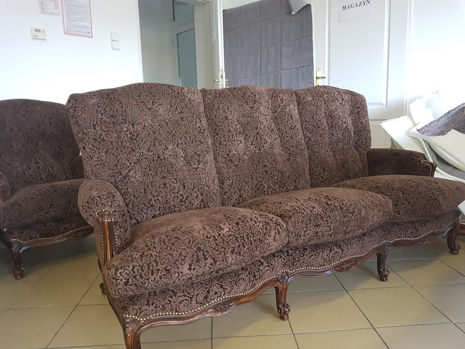 Odnowiona, brązowa sofa i fotel z ozdobnym wzorem i drewnianymi nogami, widoczne w pomieszczeniu warsztatowym z napisem 'Magazyn' na drzwiach w tle.