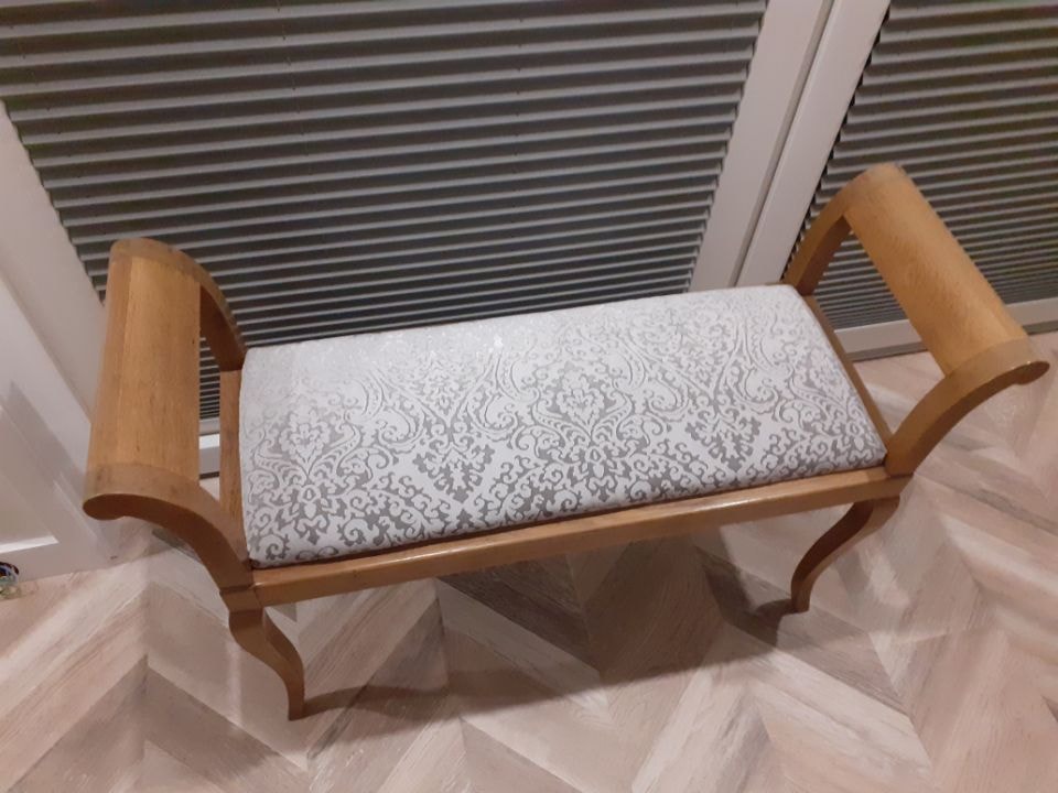 Odnowiona ławka w stylu retro z drewnianą ramą i tapicerowanym siedziskiem w kremowo-szary wzór damasceński, ustawiona na parkiecie w jodełkę, z widocznymi detalami giętych nóg i podłokietników.