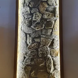 Fragment ściany wykończony kamieniem dekoracyjnym w drewnianej ramie, podświetlony od tyłu ciepłym światłem LED, na podłodze parkiet w jodełkę.