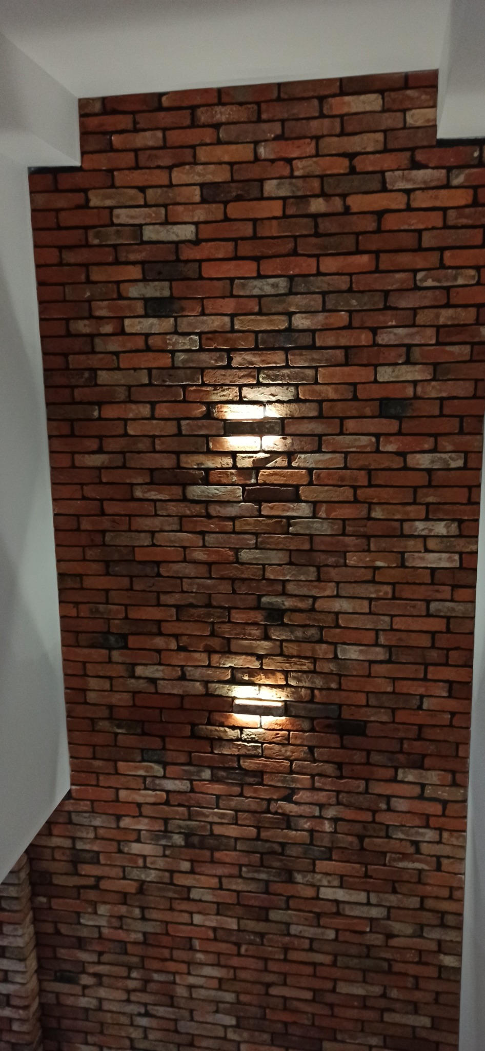 Dekoracyjna ściana z cegieł z ukrytymi punktami świetlnymi, tworzącymi ciepłą atmosferę w pomieszczeniu.