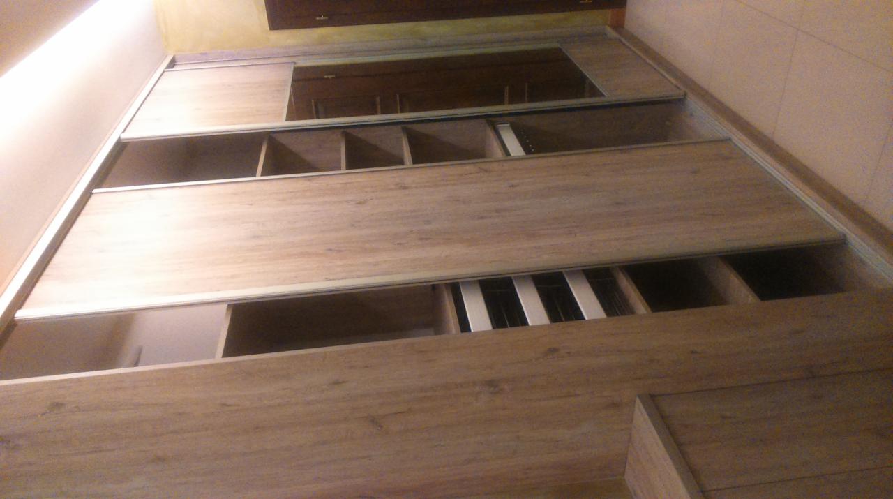 Wnętrze szafy wnękowej z przesuwnymi drzwiami w odcieniach drewna, widok z dołu, ukazujący półki i system organizacji przestrzeni.