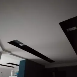 Nowoczesny sufit podwieszany z czarnymi wstawkami i oświetleniem punktowym, widok z dołu, kolumna w tle.