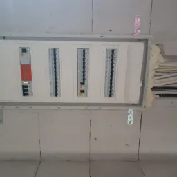 Zamontowana skrzynka elektryczna z widocznymi bezpiecznikami i przewodami, osadzona w ścianie z betonu komórkowego i uszczelniona pianką montażową.