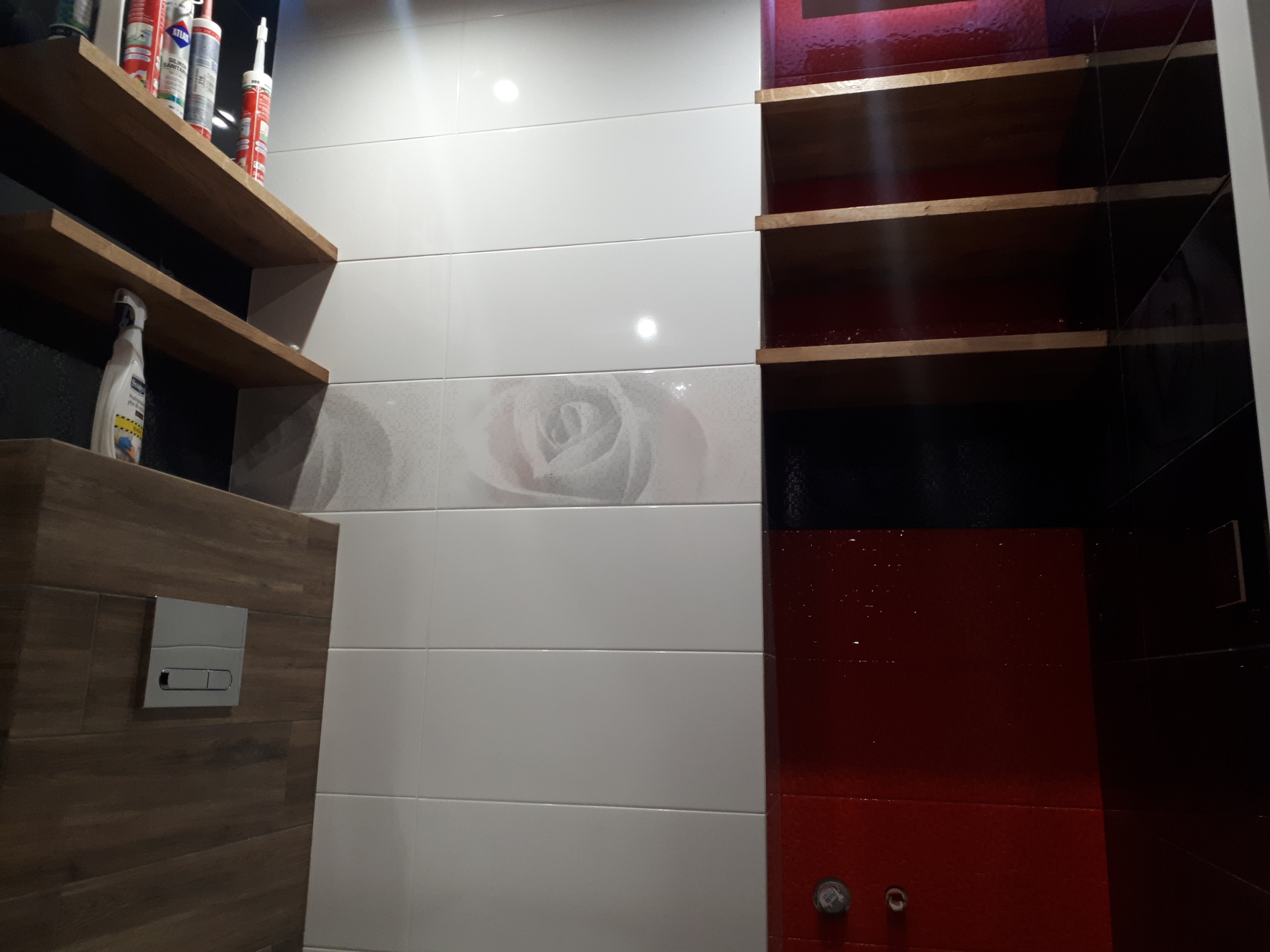 Nowoczesna łazienka z białymi płytkami z motywem róży, drewnianymi półkami z kosmetykami i czerwoną, lakierowaną ścianą z wbudowanymi półkami.