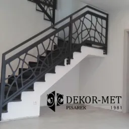 Schody z czarnymi, granitowymi stopniami i metalową balustradą o ażurowym wzorze, z logo firmy Dekor-Met Pisarek w dolnej części zdjęcia.