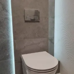 Nowoczesna toaleta podwieszana z szarą płytką imitującą kamień, podświetleniem LED i chromowanym przyciskiem spłukującym.