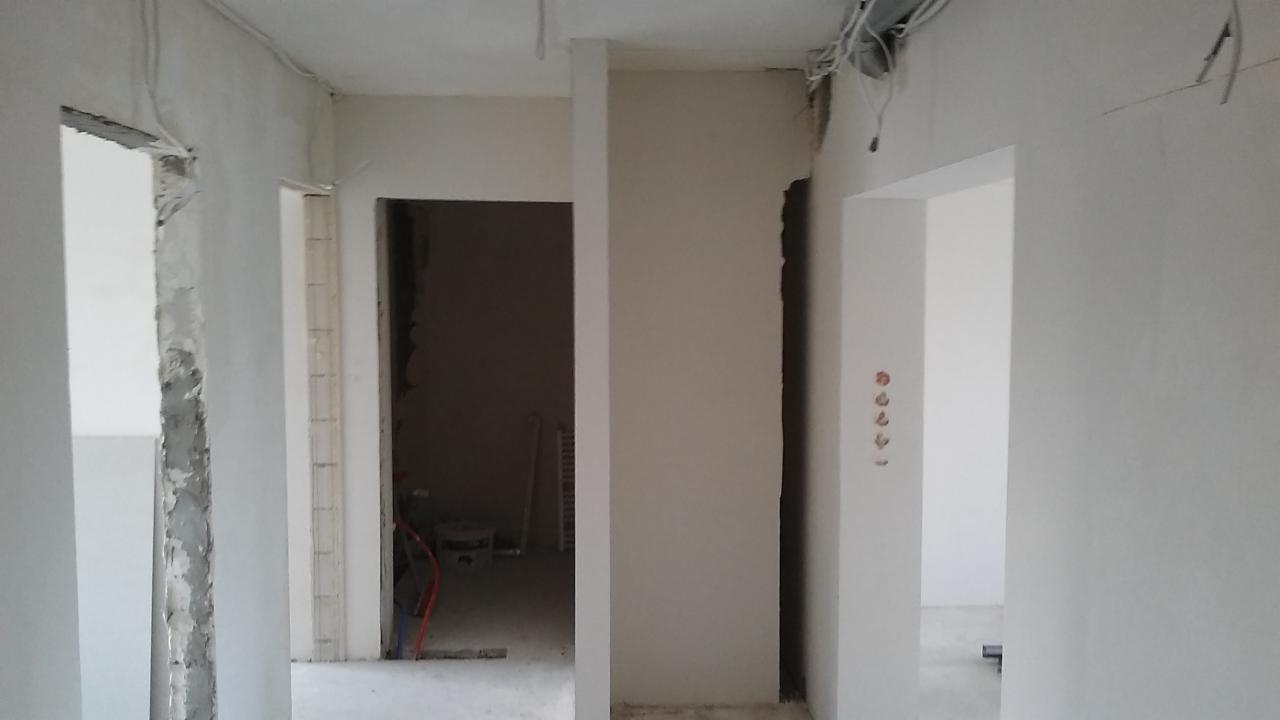 Wnętrze w trakcie remontu: ściany po szpachlowaniu i przygotowaniu pod malowanie, widoczne kable i instalacje elektryczne, surowe wykończenie ościeżnic.