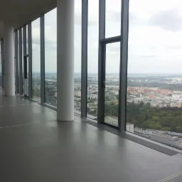 Szara posadzka żywiczna w przestronnym, wysokim pomieszczeniu biurowym z widokiem na miasto przez panoramiczne okna.