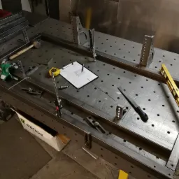 Metalowa rama w trakcie montażu na perforowanym stole warsztatowym, przy użyciu ścisków, poziomicy, rysunku technicznego i innych narzędzi.