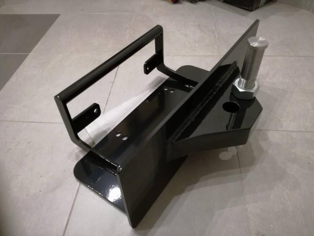 Czarny, błyszczący, spawany uchwyt z metalu z przymocowanym srebrnym trzpieniem i nakrętką, widoczne spawy.