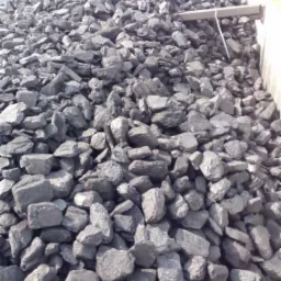 Kopalniany urobek w postaci brył węgla kamiennego, składowany w betonowym boksie, z widocznymi śladami eksploatacji i transportu.