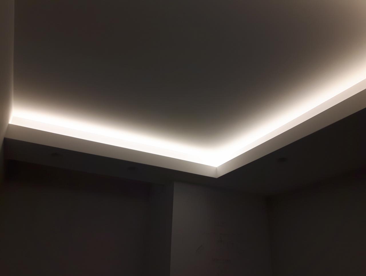 Wnęka sufitowa z oświetleniem LED, widok z dołu na narożnik pokoju z szarymi ścianami.