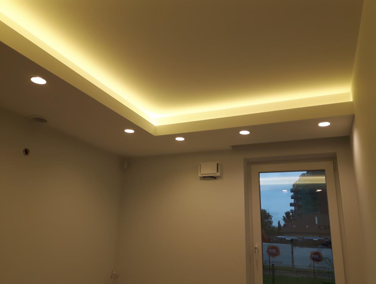 Nowoczesne oświetlenie sufitowe z listwą LED i punktowymi lampami halogenowymi w jasnym pomieszczeniu z widokiem na zewnątrz przez okno.