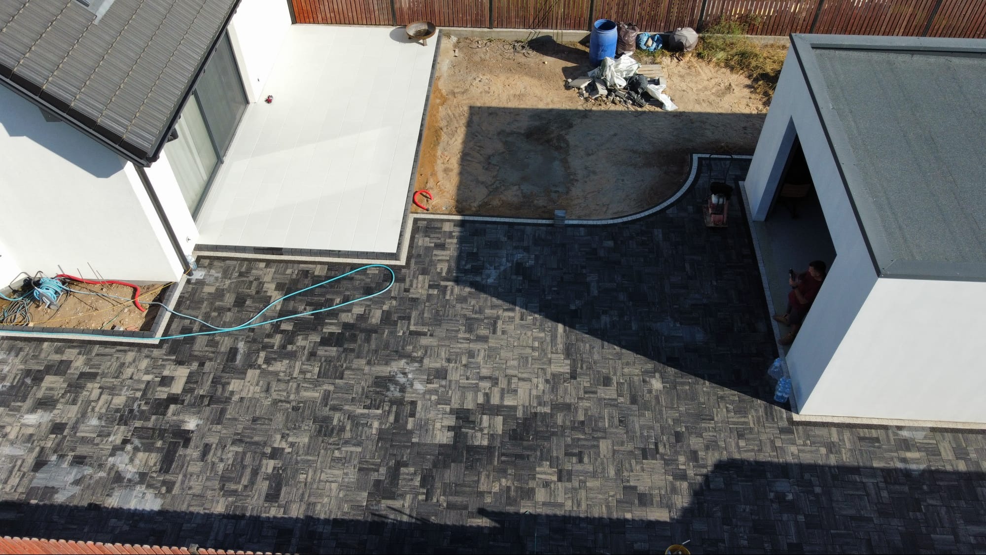 Ułożona, wzorzysta kostka brukowa na posesji z białym tarasem i przygotowanym terenem pod trawnik. Widok z góry ukazuje detale wzoru i układu kostki.