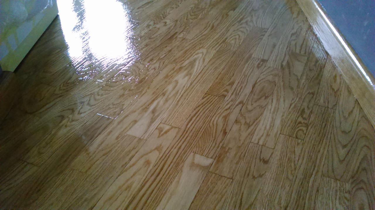 Świeżo polakierowana, błyszcząca drewniana podłoga parkietowa z widocznym usłojeniem, z listwą przypodłogową przy ścianie, odbijająca światło.