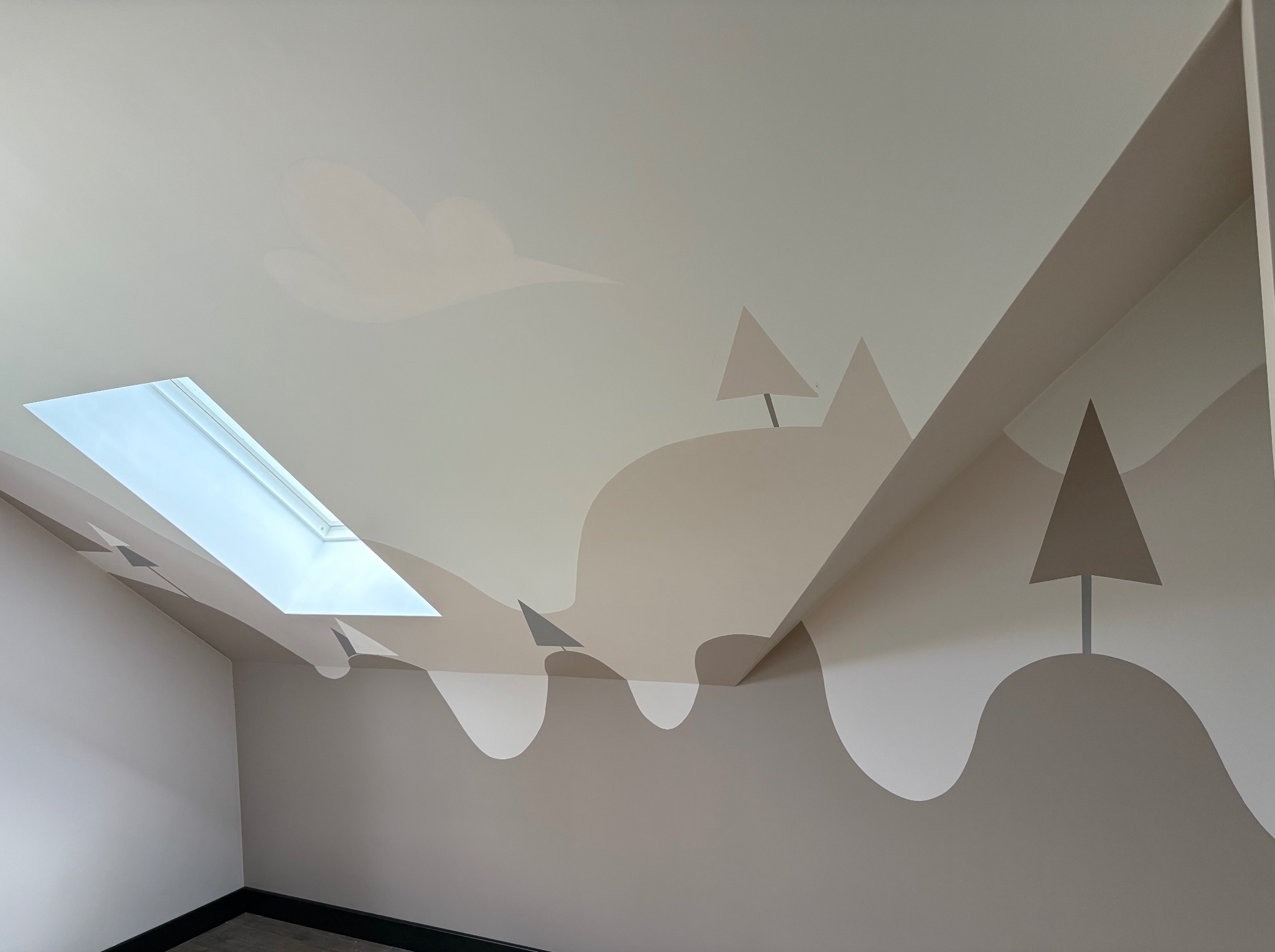 Pokój na poddaszu z pomalowanymi ścianami w motywy gór i chmur w stonowanych kolorach, oświetlony przez okno dachowe.