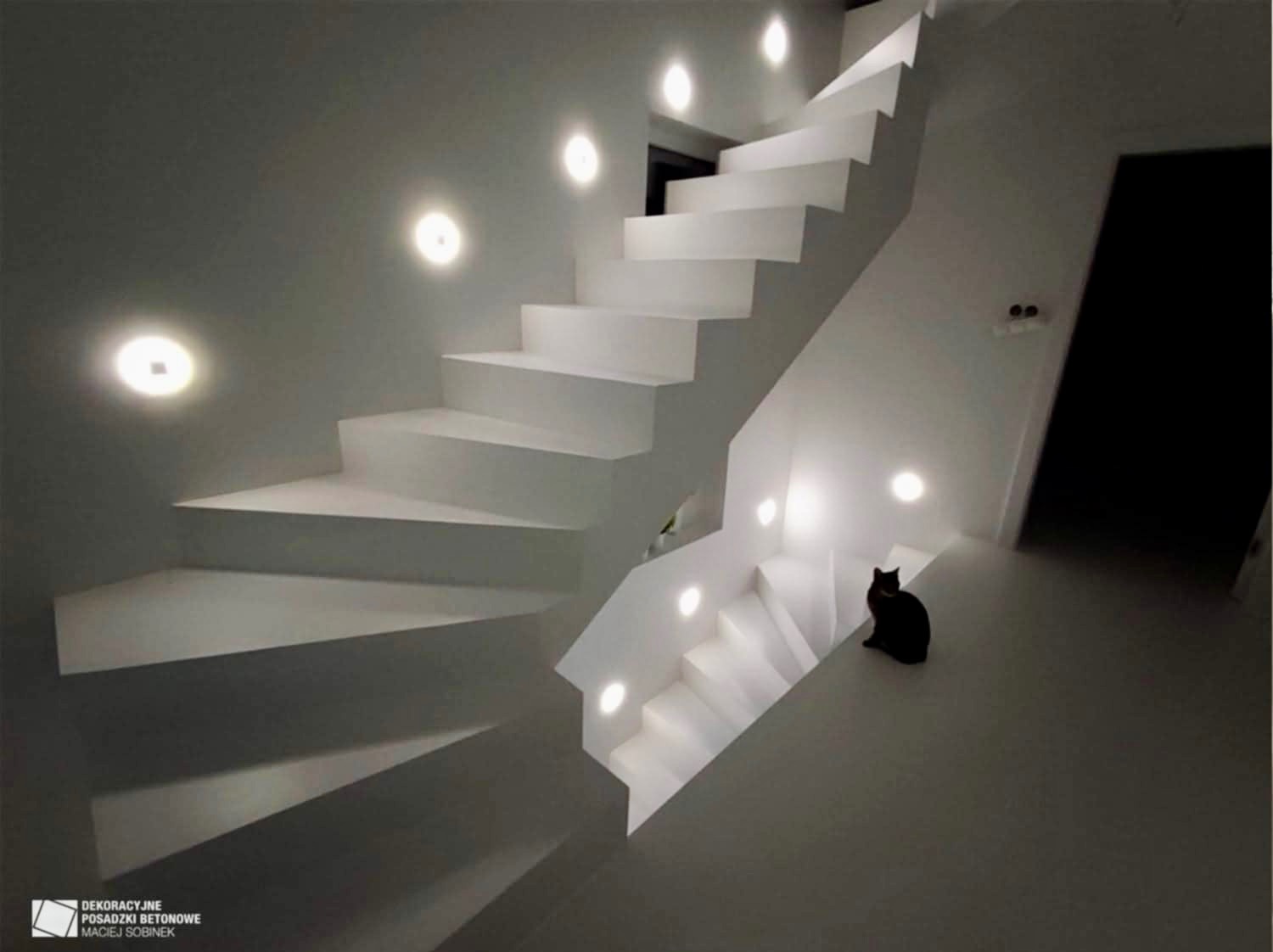 Białe schody z oświetleniem punktowym i czarnym kotem. Nowoczesne wykończenie wnętrza z dekoracyjną posadzką betonową. Minimalistyczny design.