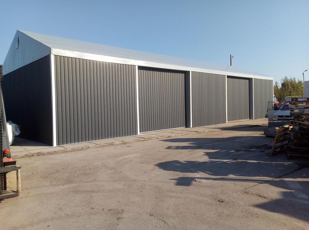 Gotowa hala magazynowa z szarymi panelami ściennymi i trzema przesuwnymi bramami, widziana z zewnątrz na betonowym placu.