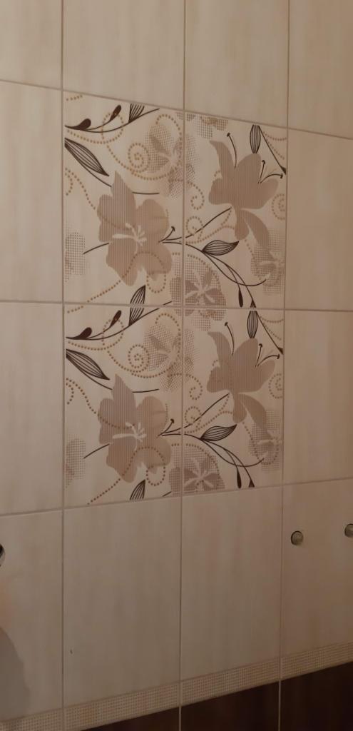 Beżowe płytki ścienne z motywem kwiatowym w łazience, widoczne otwory po instalacji.