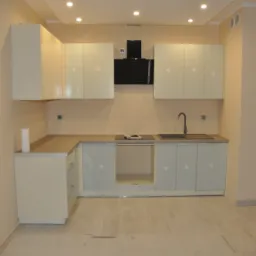 Jasna, nowoczesna kuchnia z kremowymi szafkami, czarnym okapem i drewnopodobną podłogą; widoczny fragment blatu i zlewu.