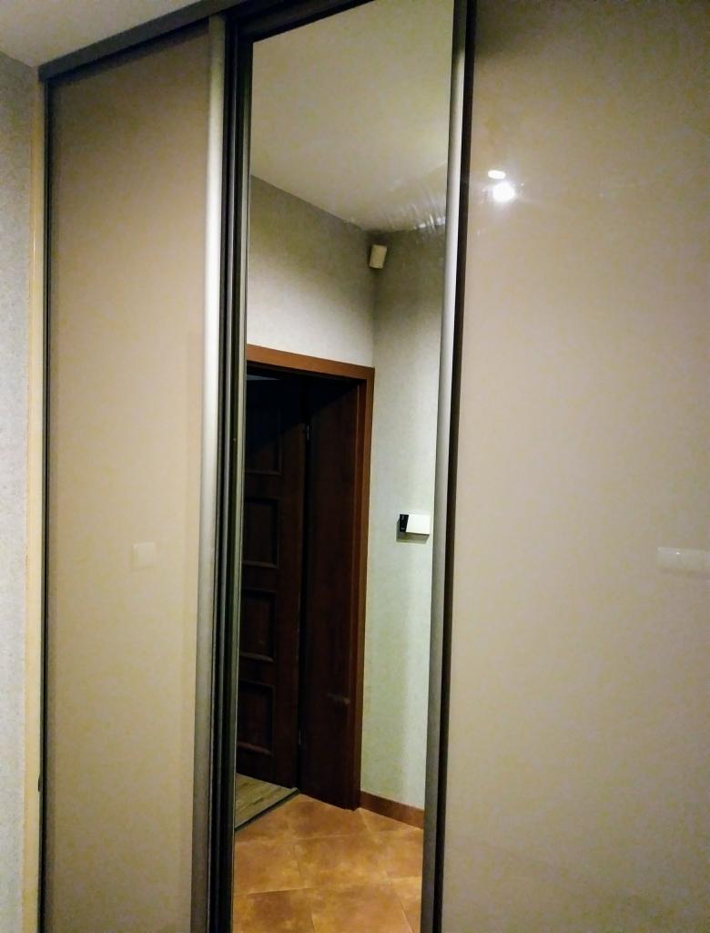 Beżowa szafa przesuwna z lustrem w korytarzu, widoczna drewniana ościeżnica drzwi i brązowa podłoga.