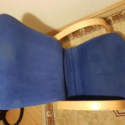 Sanpa Sp. z o.o. - Widok z góry na niebieski, pluszowy fotel z jasnymi, drewnianymi podłokietnikami, stojący na wzorzystym dywanie.